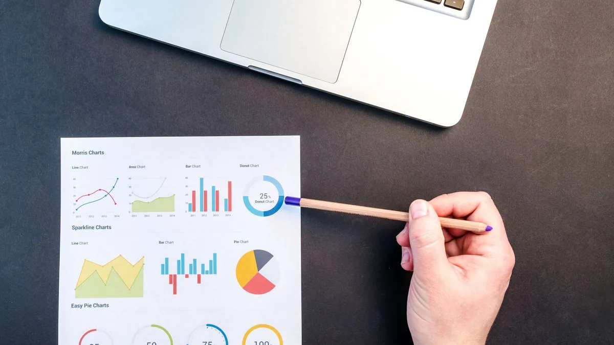 étude de marché : main tenant un crayon au-dessus de graphiques de données colorés près d'un ordinateur