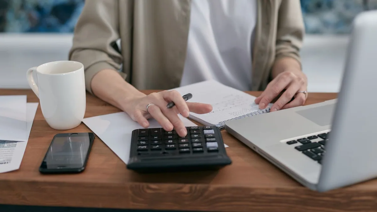 Prix hébergement site : personne calculant le budget de son site avec une calculatrice et un ordinateur